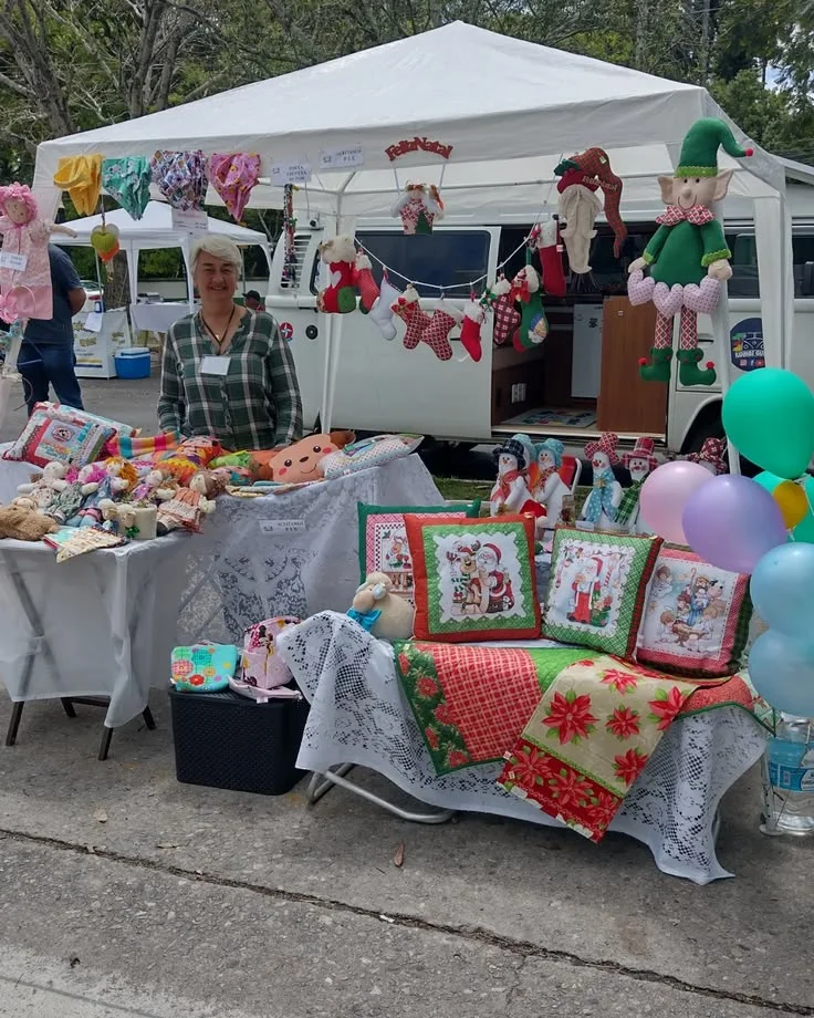 Niaia numa feira de artesanato, com peças costuradas à mão e a Kombi ao fundo